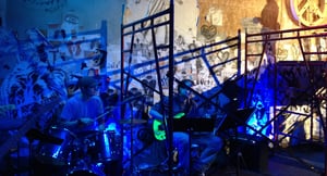 2 musicians behind a stage playing drums and guitar
